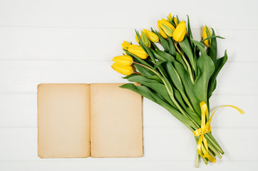 Poster - Background with yellow tulips, blank notepad on white wooden table top view. Creative woman's workspace concept with copy space. Product photograph taken from above with frame composition