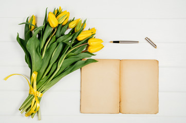 Poster - Background with yellow tulips, blank notepad on white wooden table top view. Creative woman's workspace concept with copy space. Product photograph taken from above with frame composition