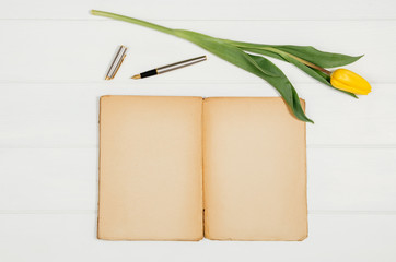 Poster - Background with yellow tulips, blank notepad on white wooden table top view. Creative woman's workspace concept with copy space. Product photograph taken from above with frame composition
