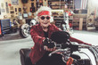 © Yakobchuk Olena - Outgoing grandmother driving motorcycle in mechanic shop