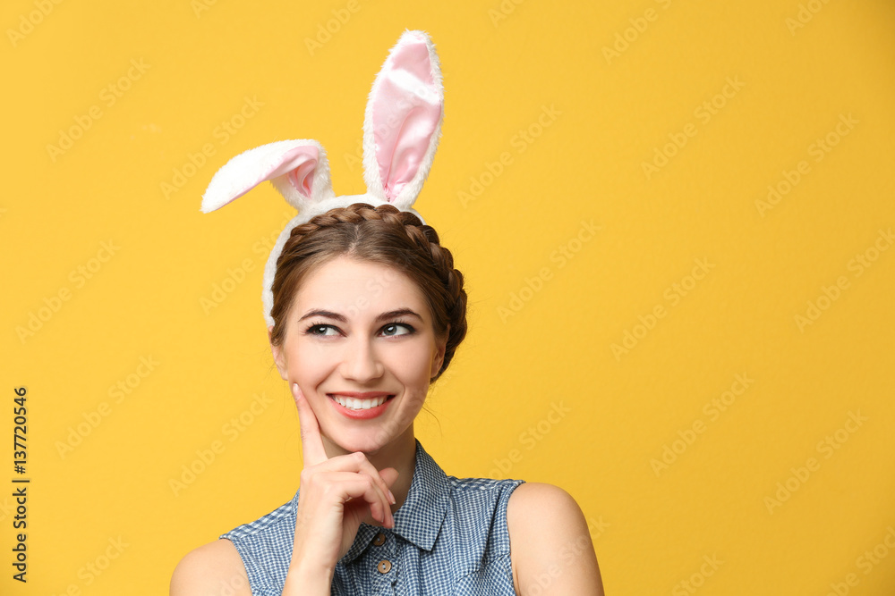 Beautiful young woman with bunny ears on color background
