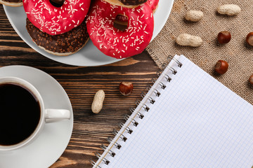 Canvas Print - Tasty donuts with cup of coffee and notebook on wooden table