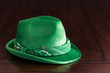 A green suede fedora hat with bandana and clover pin on the rustic wooden table.