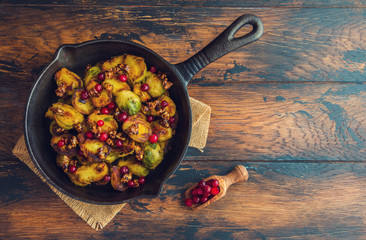 Wall Mural - Roasted Brussels sprouts with caramelized walnuts and cranberries in a cast iron frying pan on a wooden table, top view.