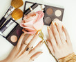 woman hands with golden manicure and many rings holding brushes, makeup artist stuff stylish, pure close up pink flower rose among cosmetic for makeup set
