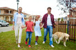 © pressmaster - Portrait of happy family with two children, boy and girl, walking their retriever dog together on green lawn in quiet residential area