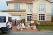 © pressmaster - Portrait of family with two children moving out: mother and daughter busy sorting personal belongings in front of house while father and son taking out cardboard boxes to van outside