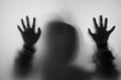© bubbers - Shadow blur of horror man in jacket with hood.Hands on the glass.Dangerous man behind the frosted glass.Mystery man.Halloween background.Black and white picture.Blur picture.