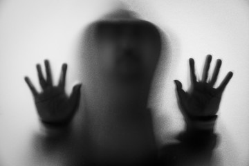 Shadow blur of horror man in jacket with hood.Hands on the glass.Dangerous man behind the frosted glass.Mystery man.Halloween background.Black and white picture.Blur picture.