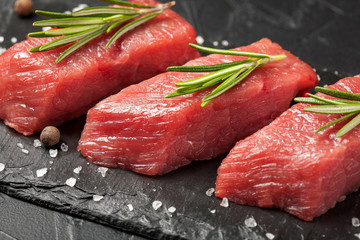 Steaks raw meat with spices on black stone background