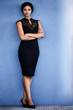 © nakophotography - Full body image of beautiful young adult black woman looking into camera with serious facial expression, with both her arms and her legs crossed, with a textured blue background.