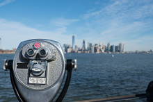 Tower Viewer Binoculars That Look Like A Face On Liberty Island With New York Harbor And The Manhattan Skyline In The Distance.  Blue Skies, Bright Beautiful Day For New York Sightseeing.