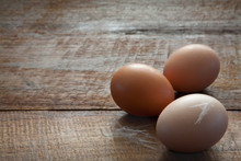 Three Fresh Farm Chicken Eggs And Feathers Close Up Horizontal On A Dark Brown Wooden Rustic Farm Table With Copy Space 
