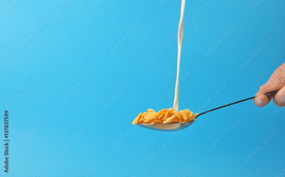 Stream of milk pouring into spoon with corn flakes