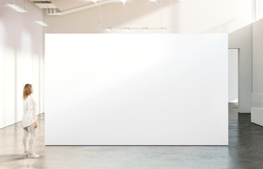 Woman walking near blank white wall mockup in modern gallery. Girl admires a clear big stand mock up in museum with contemporary art exhibitions. Large hall interior, banner exposition