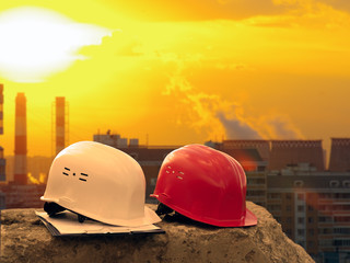 Two construction helmets on the background of the city. Homes, pipe, sunset