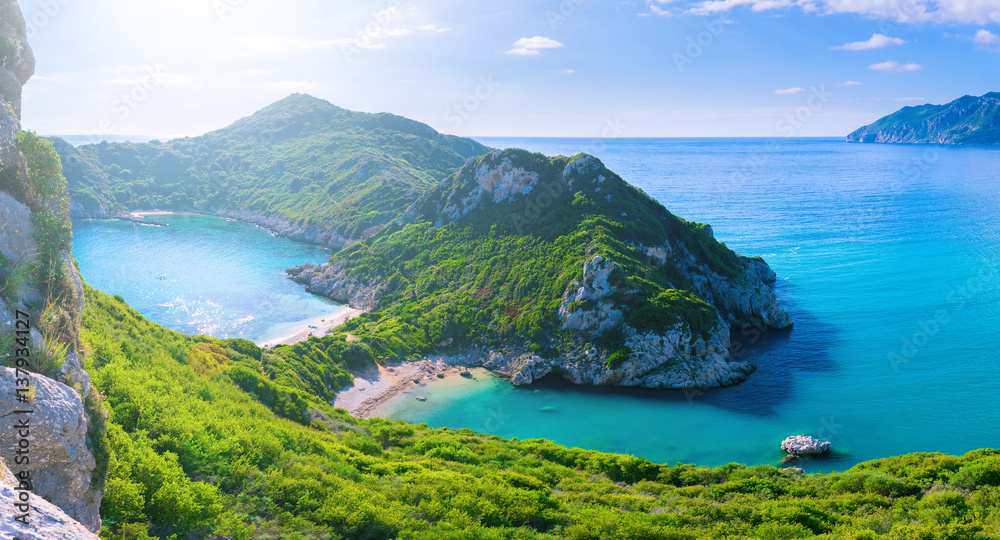 Beautiful summertime panoramic seascape. View of the cliff into the crystal clear azure sea bay and distant islands. Unique secluded beach. Agios Stefanos cape. Afionas. Corfu. Greece. - obrazy, fototapety, plakaty 