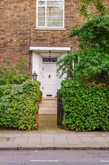 the entrance to a building stone steps on botj sides green vegetation, white window, peak at the entrance, two stylish lamps on both sides of the entrance, a beautiful white wood doors