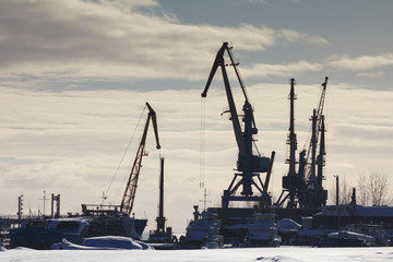  View of seaport at sunny winter day - cargo cranes in ice harbor, silhouette