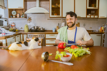 Wall Mural - a man cooks in the kitchen beside him sits a funny beautiful cat
