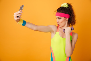 Canvas Print - Happy playful young woman athlete holding dumbbell and taking selfie