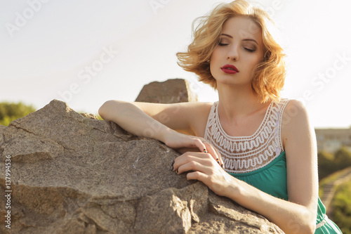 Fotografía Beautiful blonde woman with curly short bob hairstyle, delicate make up and red lips in green short dress at the park