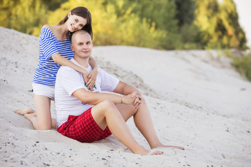 Happy smiling family couple of slim fit beautiful brunette mother and bold fat father and on a park in blue, white and red outfit: t-shirt and shorts. Summer sunset. Copy space