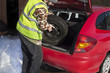 Mężczyzna wyciąga koło zapasowe z bagażnika samochodu ubrany w kamizelkę odblaskową. Wymiana koła zapasowego w warunkach zimowych