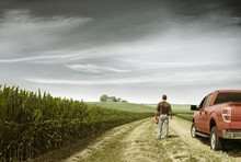 Rear View Of Farmer Standing By Car On Field Against Cloudy Sky