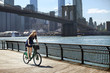 © Cavan Images - Woman cycling on promenade against Brooklyn Bridge