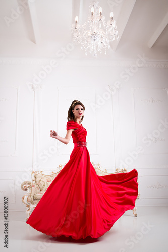 Elegant woman in a long red dress is standing in a white room chic, swirl dress Poster