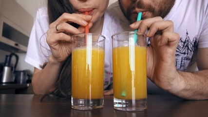 Young woman and man drinking orange juice with straws together. Healthy lifestyle or funny competition concepts