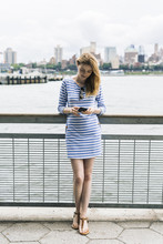 USA, New York City, Young Woman Standing In Manhattan Using Smart Phone