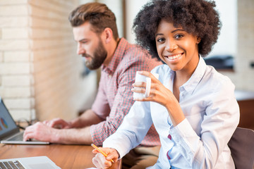 Wall Mural - Beautiful african businesswoman and caucasian man working together with laptops and coffee cups near the window at the cafe or office