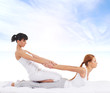© Acronym - Young woman getting traditional Thai stretching massage by therapist over sky background