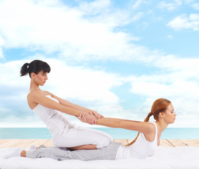 Wall Mural - Young woman getting traditional Thai stretching massage by therapist on a pier