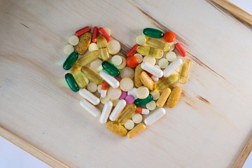 Heart of pills for treatment on a wooden board. Treatment of heart pills at home. A lot of pills on the table