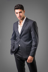 Wall Mural - Young businessman confidently posing in front of camera, wearing business suit without neck-tie, with shirt open on neck, on dark background