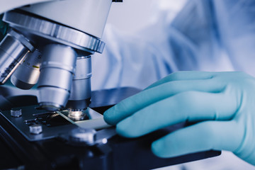 Wall Mural - close up view of scientist hands with gloves set the sample in the microscope for research