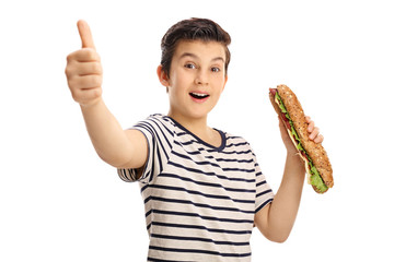 Joyful young boy holding a sandwich and giving a thumb up