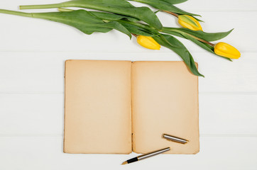 Poster - Background with yellow tulips, blank notepad on white wooden table top view. Creative woman's workspace concept with copy space. Product photograph taken from above with frame composition
