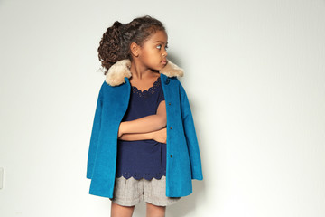 Cute little African American girl in coat against light wall. Fashion concept