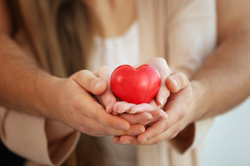 Young couple holding small red heart, closeup