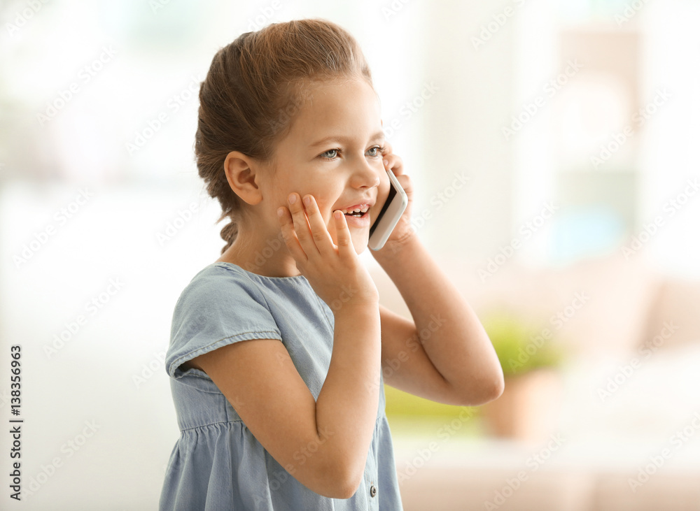 Cute little girl talking by mobile phone at home