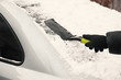 Man removing snow from car with scraper