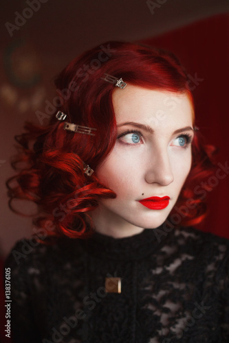 A Woman With Red Curly Hair In A Black Dress And Retro Makeup On A Red