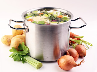 Broth with carrots, onions various fresh vegetables in a pot - colorful fresh clear spring soup. Rural kitchen scenery vegetarian bouillon or stock