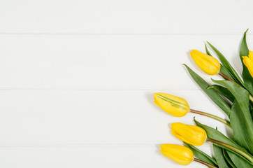 Poster - Background with yellow tulips on white wooden table top view. Creative woman's workspace concept with copy space. Product photograph taken from above with frame composition