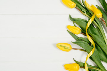 Poster - Background with yellow tulips on white wooden table top view. Creative woman's workspace concept with copy space. Product photograph taken from above with frame composition