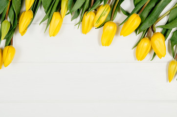Poster - Background with yellow tulips on white wooden table top view. Creative woman's workspace concept with copy space. Product photograph taken from above with frame composition